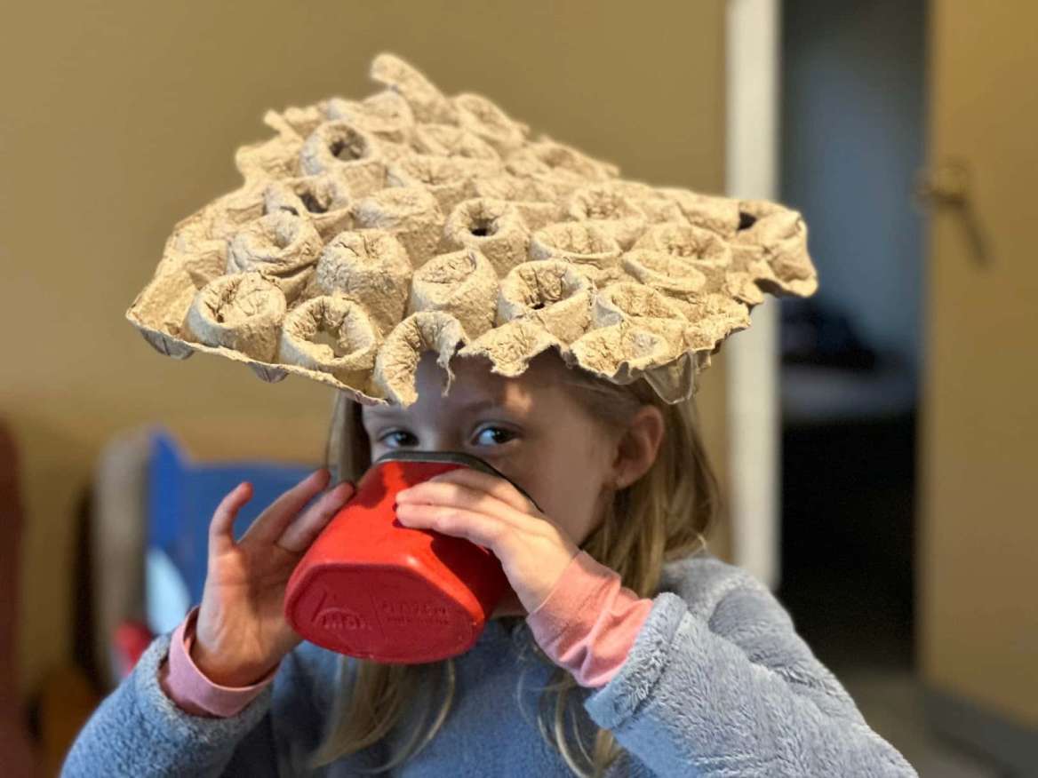 A Beaver Scouter having some hot chocolate while wearing an egg carton hat.